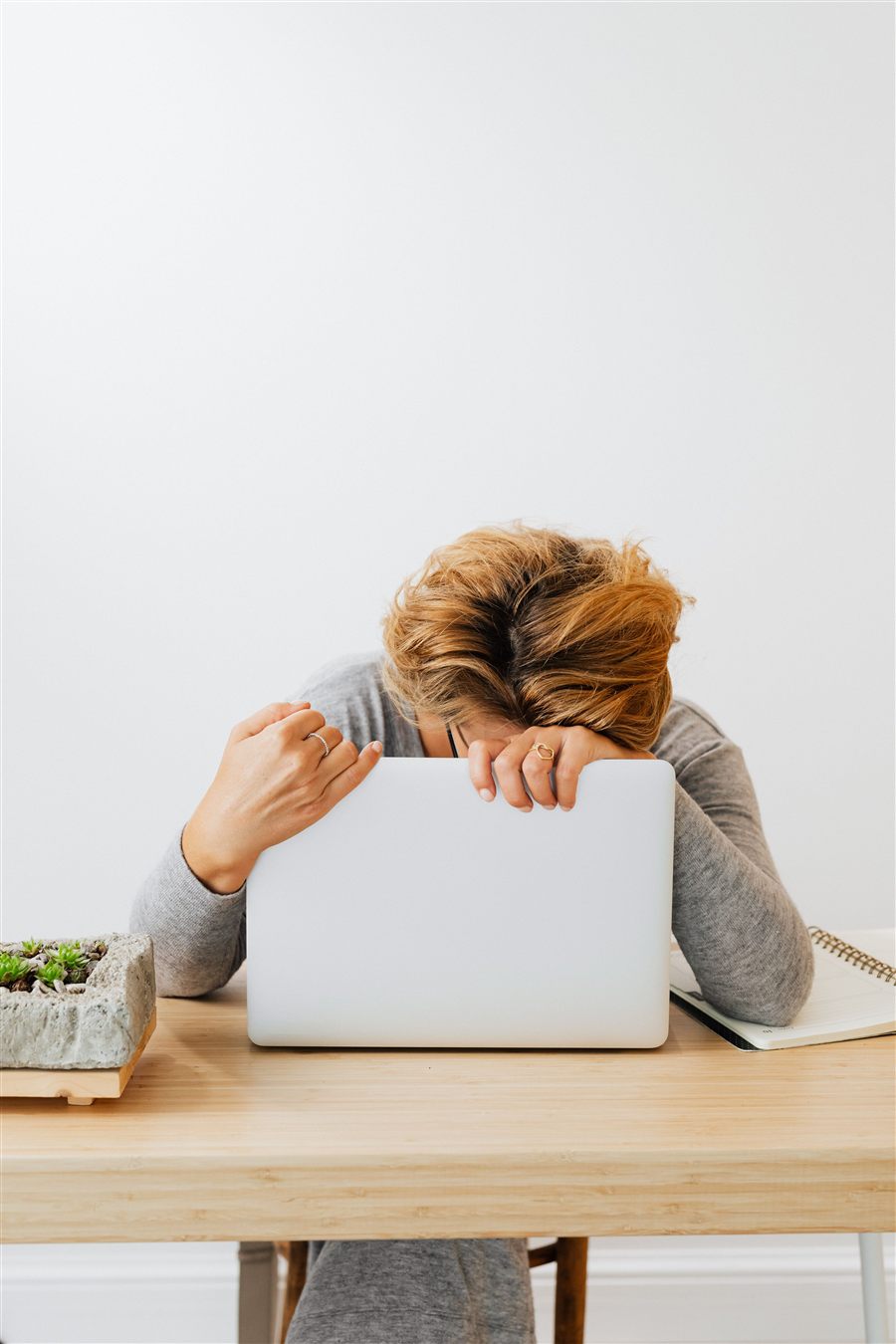 Zmęczona kobieta opiera głowę o laptop - zmęczenie dawaniem ponad siły